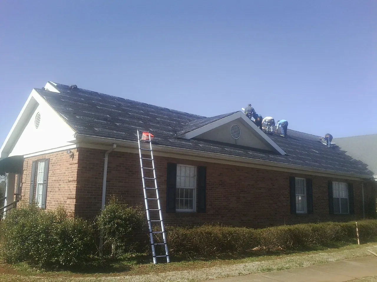 Crew tearing shingles off a brick ranch roof with a ladder set — Emergency Roof Repair work by our crew in Rebuck