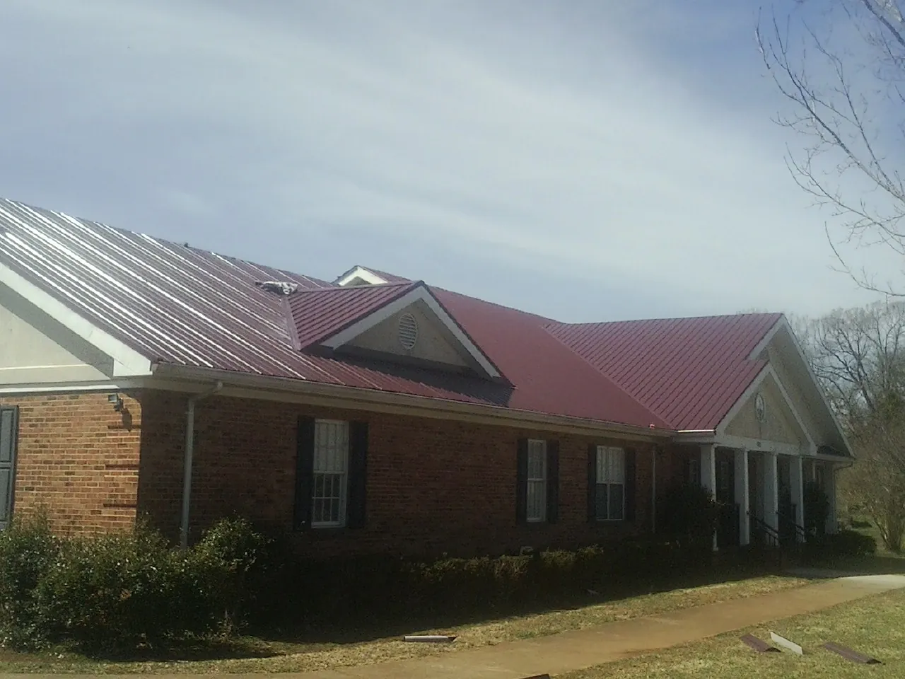 Red metal roof with gabled entries on a long brick building, from a Hail Damage Roof Repair job in Rebuck