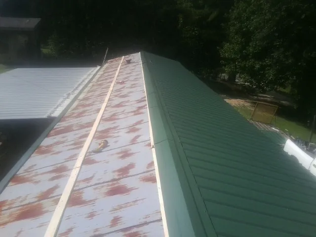 Old rusted panels beside newly installed green metal roofing — Wind Damage Roof Repair by Roofing Brothers in Rebuck