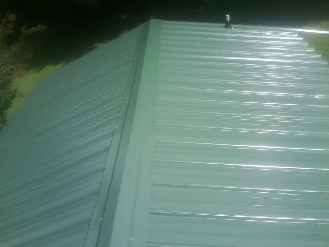 New green metal panels meeting at the ridge of a roof — Flat Roof Repair work by our crew in Rebuck
