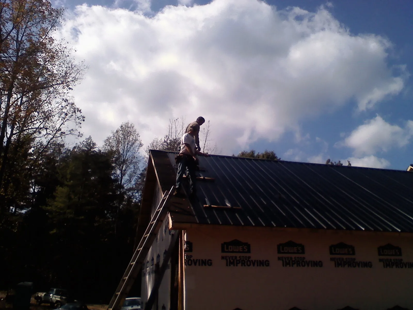 Roofer fastening dark metal panels high against a cloudy sky, from a Roof Inspection job in Rebuck
