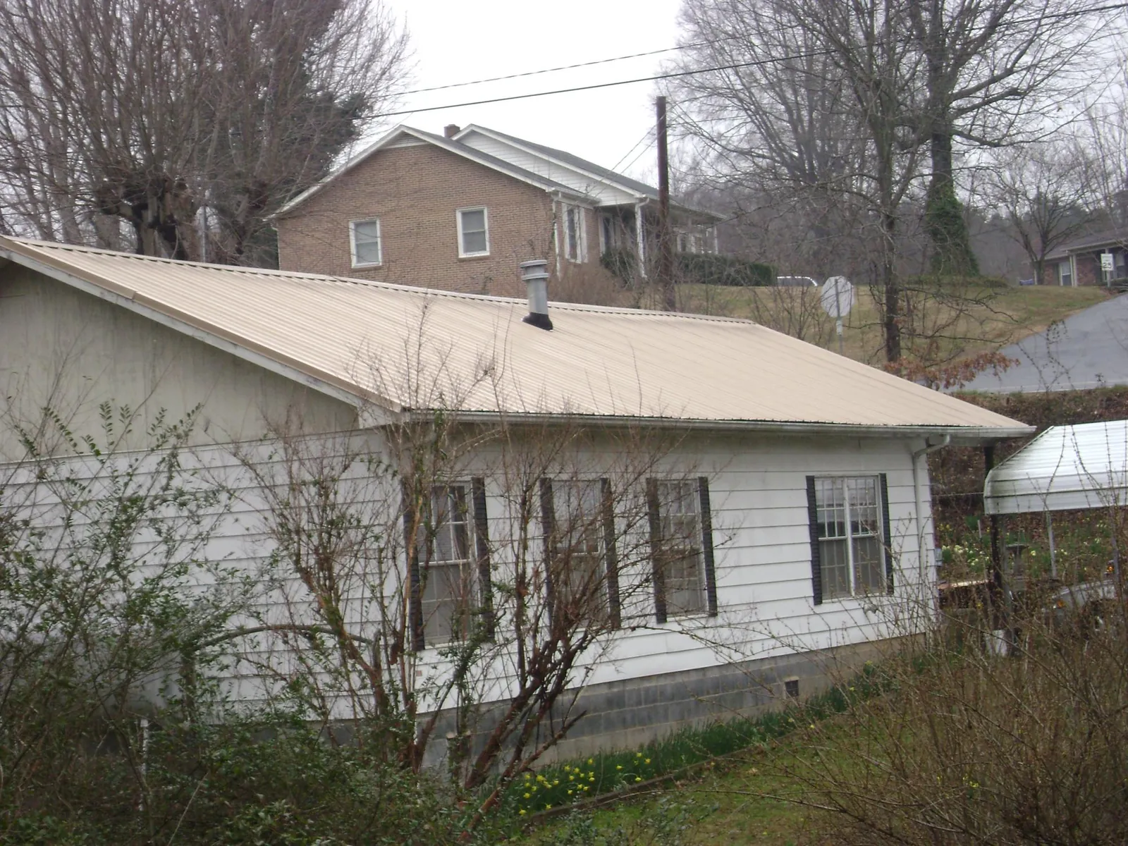Tan metal roof on a white sided house set into a hillside — Commercial Roofing by Roofing Brothers in Rebuck