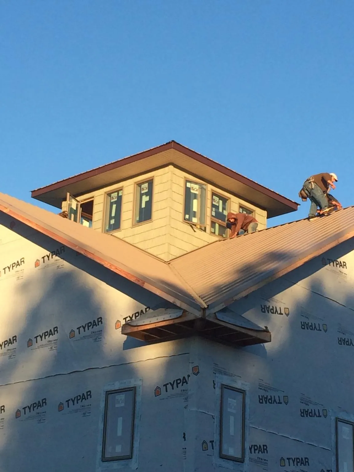 Roofers working around a rooftop cupola on a new metal roof at sunset — Roof Waterproofing in Rebuck by Roofing Brothers